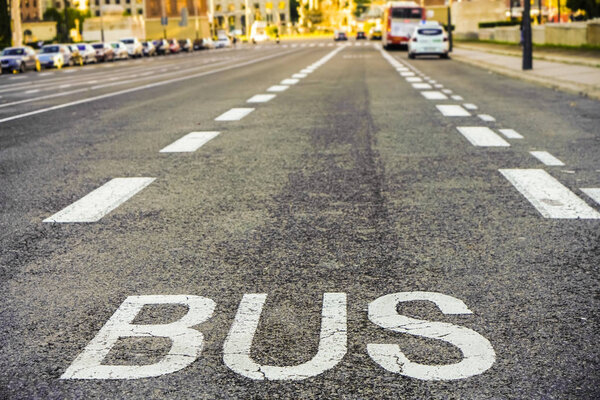 view of word " BUS " written on asphalt street road. car parking along way. 