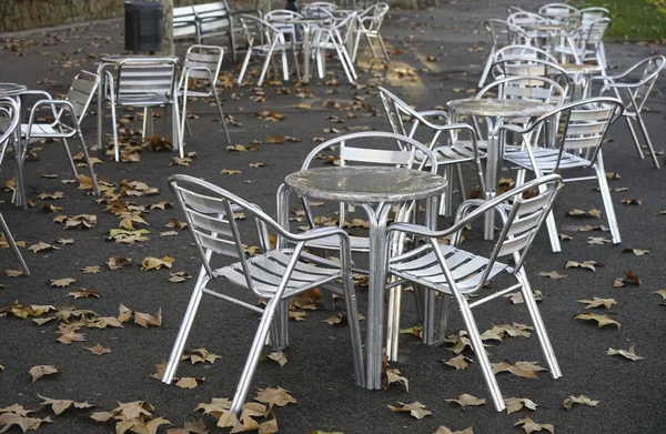 outdoor empty summer cafe - metal tables and chairs. fallen leaves on floor. autumn season.