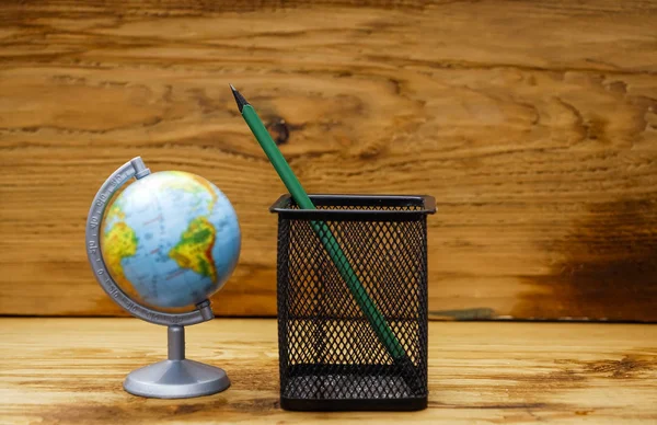 one green pencil in metal net case and globe against wooden background. back to school