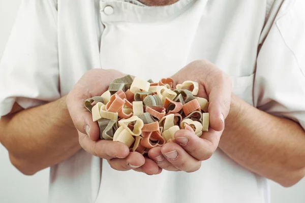 male chef holding heart shaped red, green and white raw pasta.