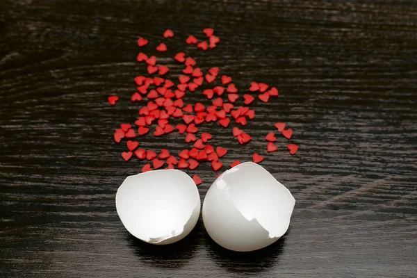 two parts o Egg shell and many red hearts on the wooden board background.