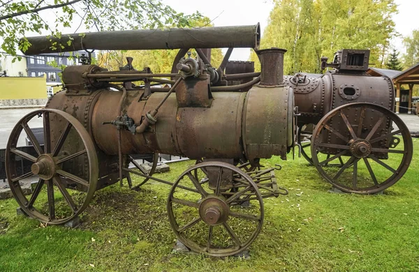 View of the antique rusty agricultural locomobile. Old and rustic steam train or tractor. Made in England. Old fashioned steam tractor standing in a field. Old Vintage Steel Wheel Farm tractor.