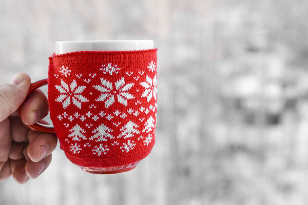 male hand holding red cup over winter pine forest background 