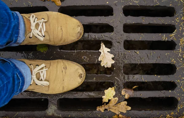 Male leather Shoes on drain cover with falling yellow and brown oak leaves. autumn cleaning in the park. — Stock Image Male Leather Shoes Drain Cover Falling Yellow Brown Oak Leaves Stock Picture