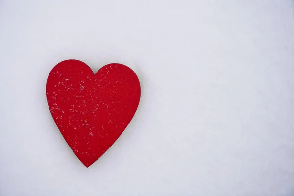 red wooden heart on  white artificial snow with snowflakes