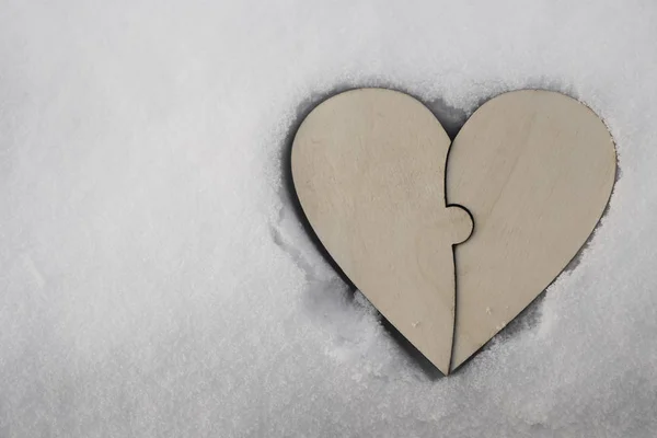 one wooden heart  from two pieces of puzzles on white snow background. empty copy space for inscription.