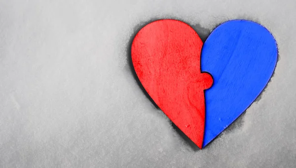 one wooden heart  from two pieces of puzzles on white snow background. empty copy space for inscription.