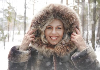 Orta yaş gülümseyen kadın kahverengi kış ormandaki açık havada manzarayı kat aşağı kapüşonlu giyiyor. 