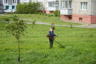Çimleri biçen bir bahçe işçisi. Çimenlikte çalışan general üniformalı adam.. 