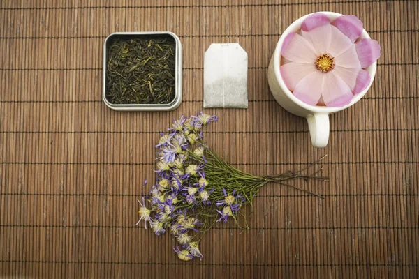 red flower in tea cup, dry green tea grass, leaves, dry blue flowers lie on brown background. top view. Herbal decoction - Imag