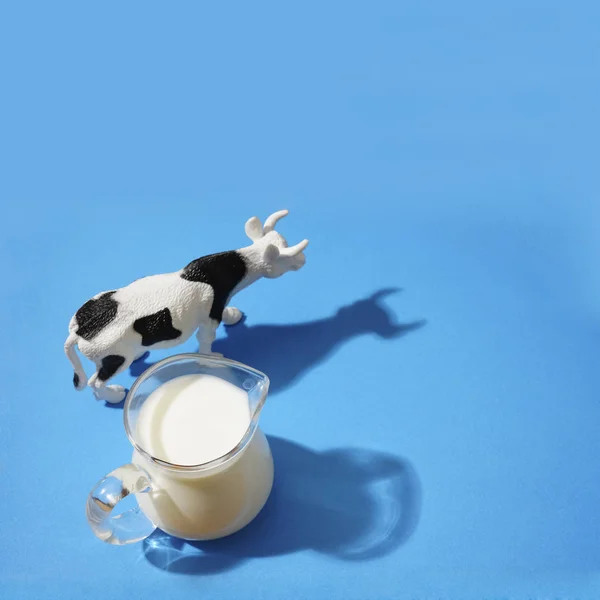 full milk jugful and cow toy  isolated on blue background. light and shadow. empty copy space for inscription.