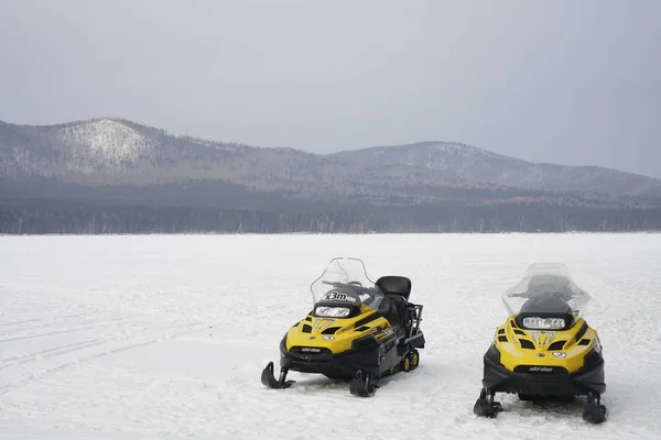 Dois Snowmobiles Amarelos Que Estão Gelo Contra Floresta Montanhas Fundo — Fotografia de Stock