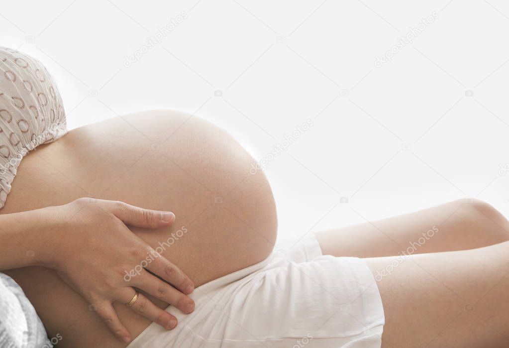 Unrecognizable pregnant woman - close-up of belly on white window background. pregnant on couch at home. no face. 