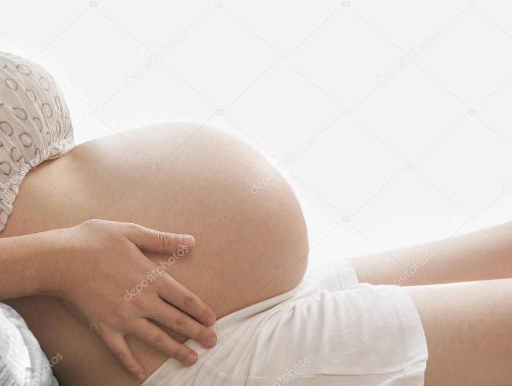 Unrecognizable pregnant woman - close-up of belly on white window background. pregnant on couch at home. no face. 