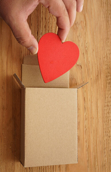 male hand holding  one red heart above open gift box on  wooden background. happy Valentines day. 14th February.   