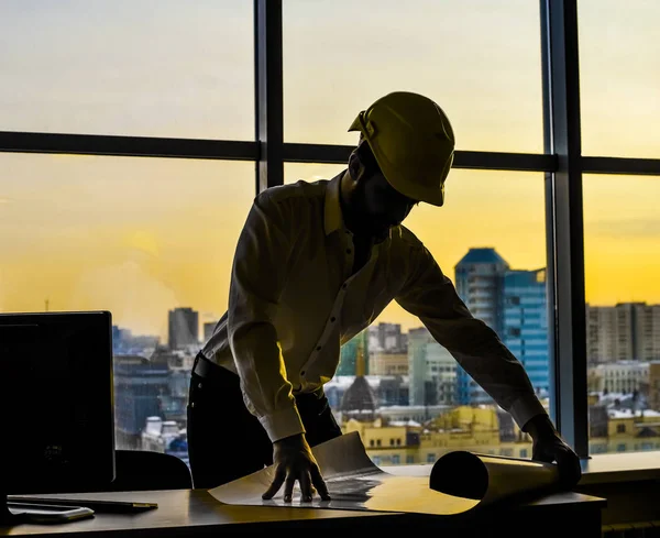 Silhouette builder engineer wear security helmet looking  at blueprint paper construction drawing plan