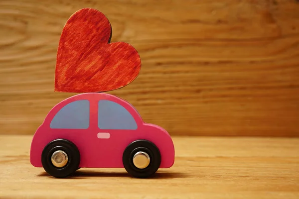 Wooden car with a little wooden red heart figure isolated on wooden board background.