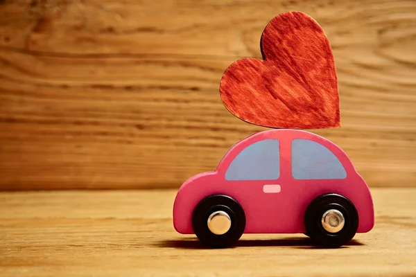 Wooden car with a little wooden red heart figure isolated on wooden board background.