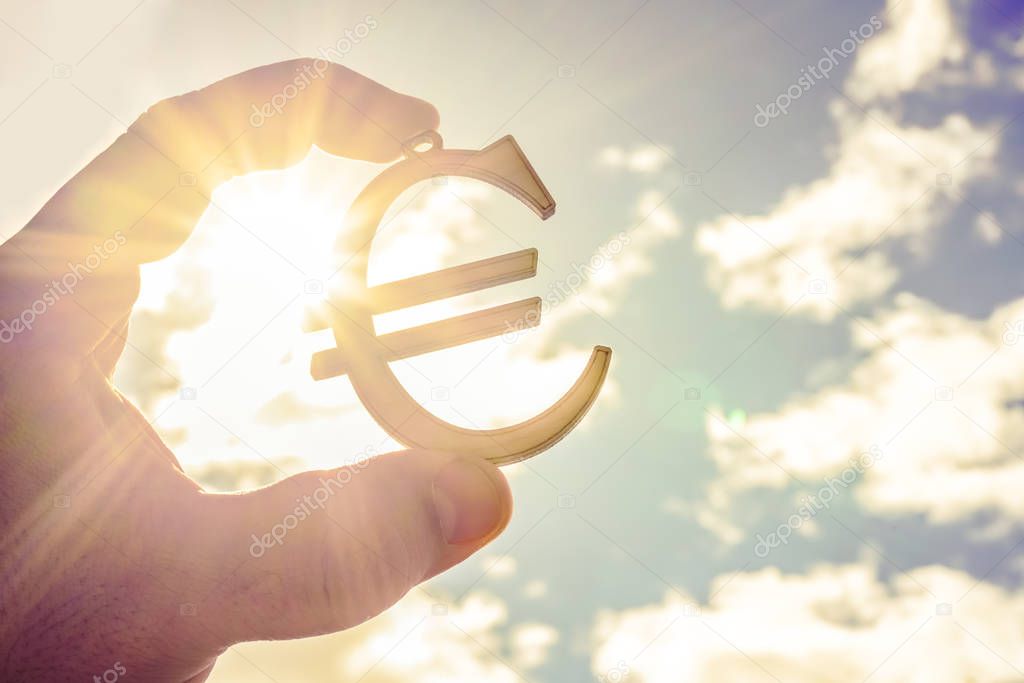 man's hand holding  wooden Euro sign against blue  sky. 