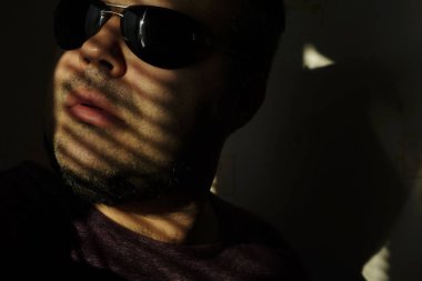 Vitrinlere bakıyor güneş gözlüklü adam; Şerit Gölgelerin içinden güneşlikler