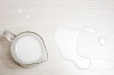 glass jug of milk on a wooden background. top view. spilled milk.  clipart