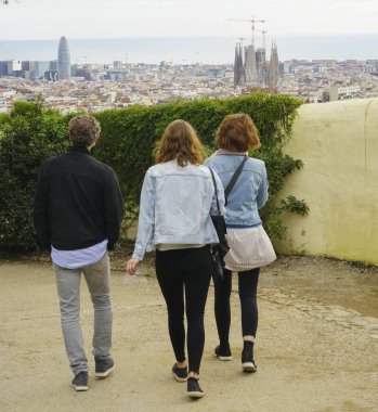 Barselona, İspanya - 25 Kasım 2018: Üç turist, Barselona şehri ve Akdeniz manzarasına karşı parkta yürüyor. 