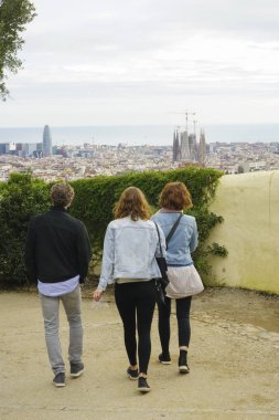 Barselona, İspanya - 25 Kasım 2018: Üç turist, Barselona şehri ve Akdeniz manzarasına karşı parkta yürüyor. 
