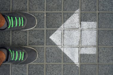Cobblestones ayağa. gri spor ayakkabı beyaz ok boyama ile yolda. 