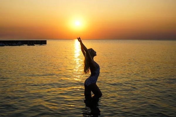 Happy fit woman stretching hands up on the beach with beautiful sunset.