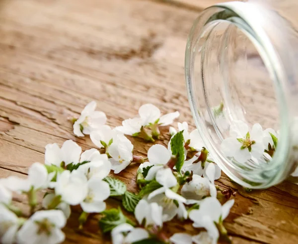 bouquet of white spring flowers and  transparent jar on wooden table background.
