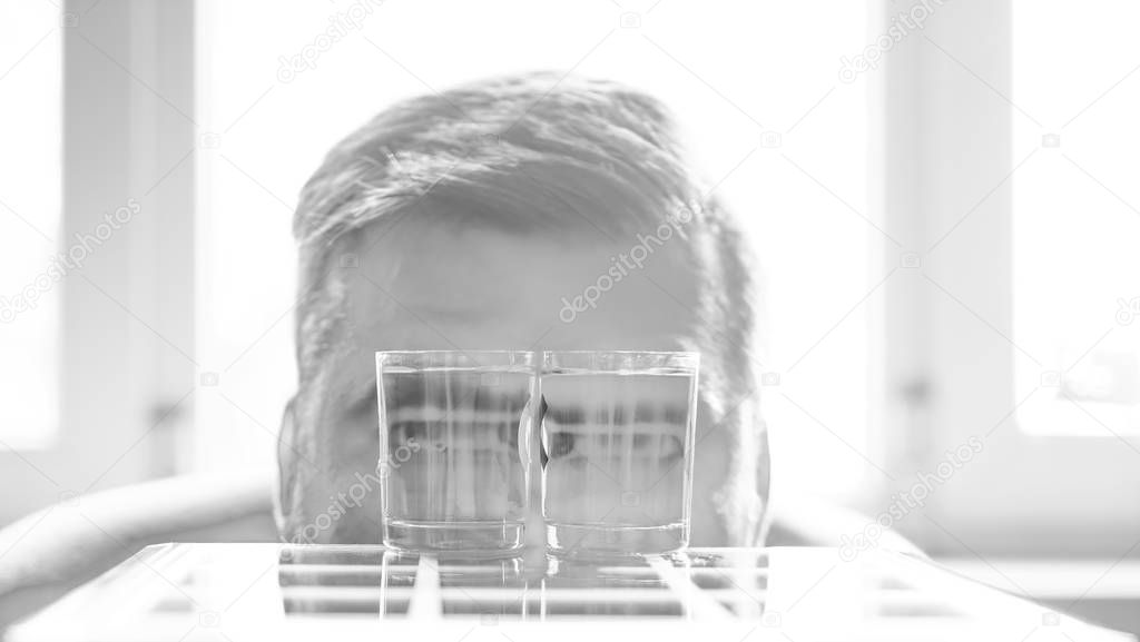 man with two glasses.  eyes magnified in the glasses filled with water.