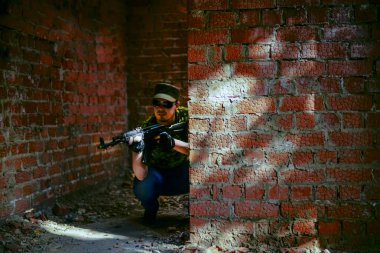 duvara odaklanın. Siyah güneş gözlüğü kapalı kentsel oda alanı beyaz askeri adam terk edilmiş kırmızı tuğla duvar yakınında makineli tüfek ile standı. Alacakaranlık ışığı. Perspektifte koridor. Yazıt için boş alan