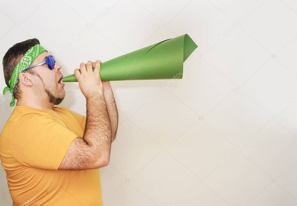Young stylish man screaming emotionally in paper trumpet, megaphone isolated on gray or white wall. 