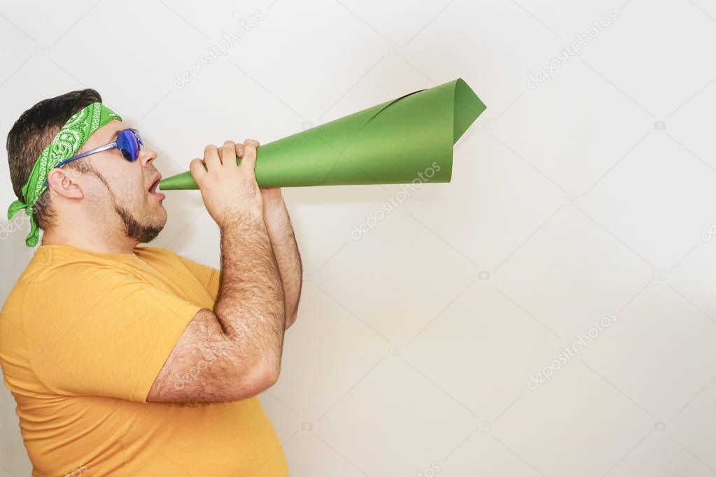 Young stylish man screaming emotionally in paper trumpet, megaphone isolated on gray or white wall. 