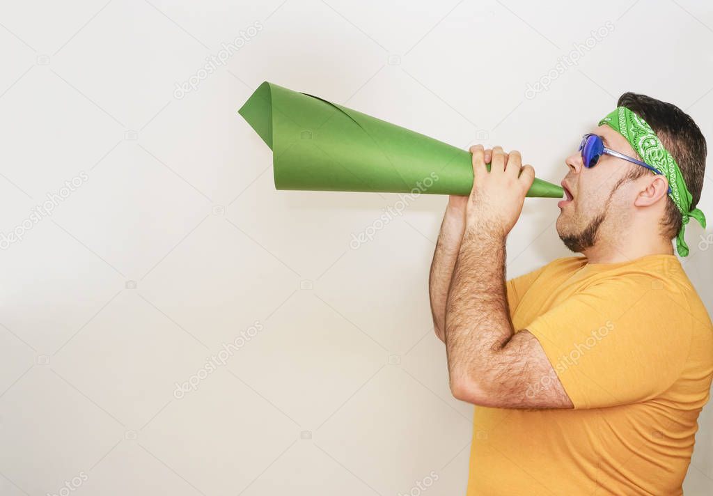 Young stylish man screaming emotionally in paper trumpet, megaphone isolated on gray or white wall. 