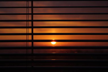 Yatay panjurların arkasında gün batımı güneşi, makro çekim. kirli cam