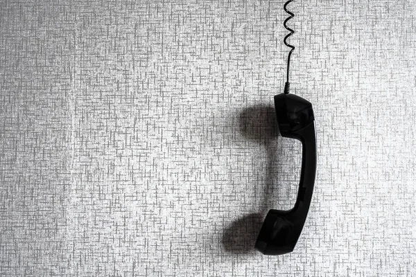 black old handset with a wire hanging  against wallpaper texture.