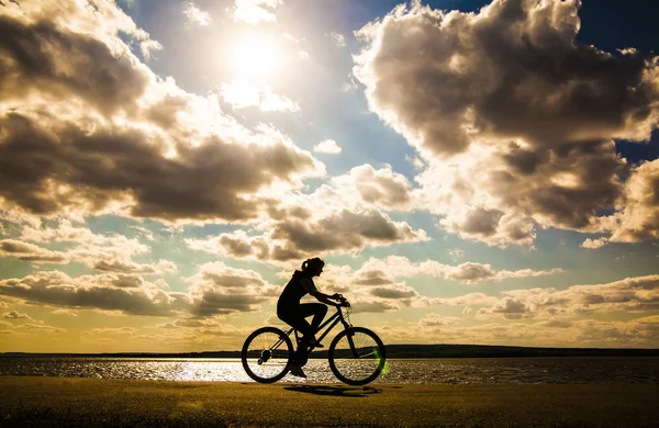 sporty  tourist woman  on  the bike against sunset sky with clouds and sun rays.