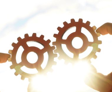 metal dişliler tutan iki Erkek eller - gökyüzü arka plan. iş, etkileşim, takım çalışması fikri