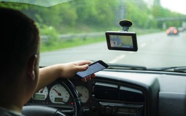 Arabanın ön koltuğunda oturan akıllı telefon kullanan adam. Ekrana odaklanmış arka görünüm.  