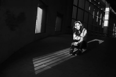 Neşeyle dinleniyor. Güzel genç kadın müzik dinliyor ve otoparkta yerde oturuyor. güneşli ışık ve yüzünde gölgeler