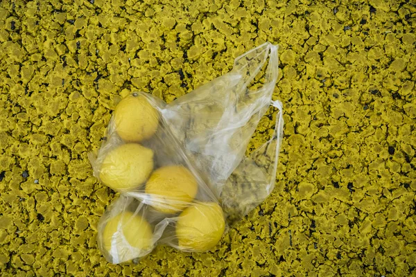 a lot yellow lemons in a transparent packaging bag lie on asphalt road.