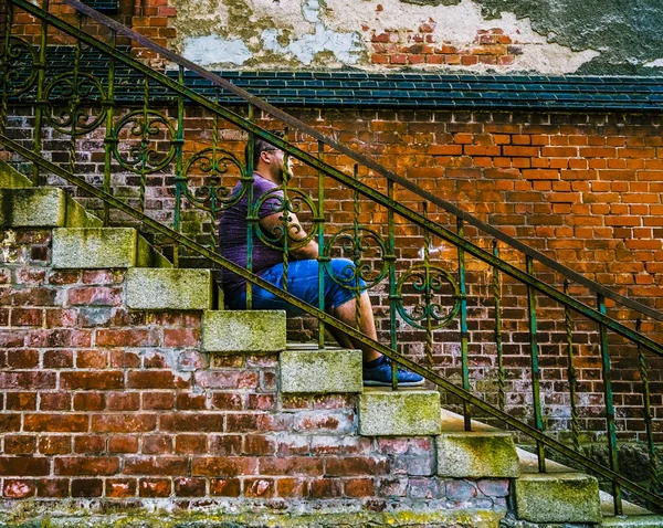 レンガ造りの建物の背景の階段に座っているハンサムなペンシブな男 レンガの壁の近くに座ってうつ病の若いブルネットの男の肖像画 — ストック写真