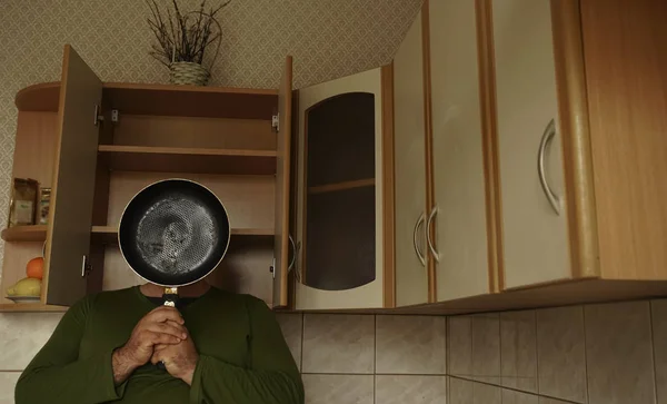 A young man covering his face with a frying pan. Photo taken at home kitchen.