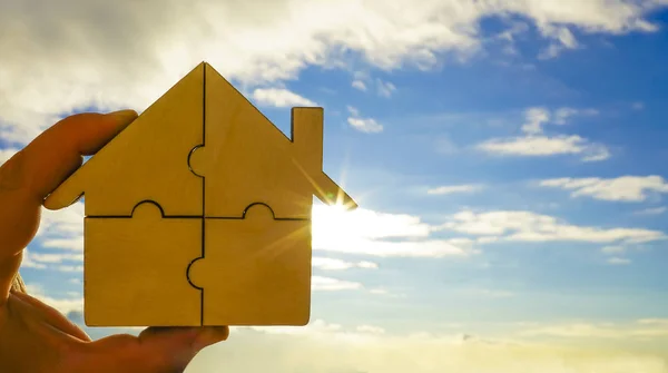 hand holding   wooden house puzzle on blue  sky background.