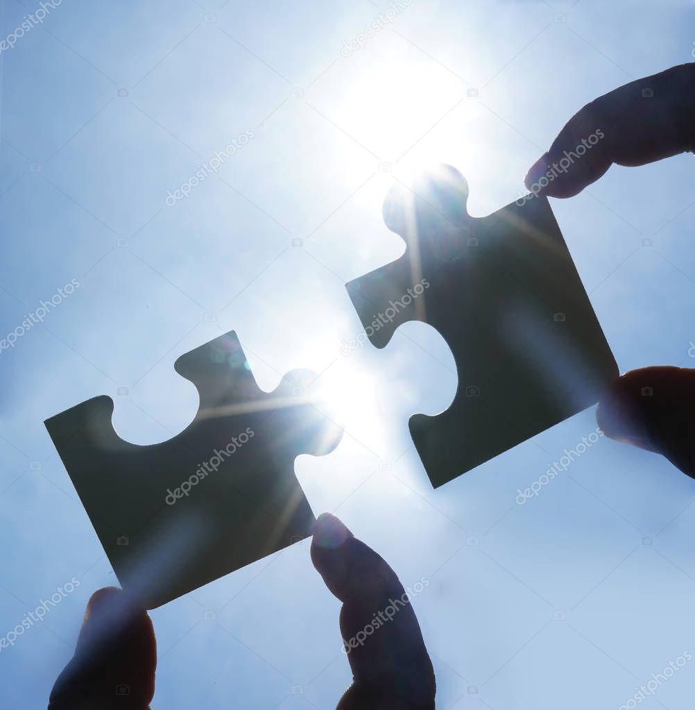 two hands trying to connect couple puzzle piece with sunset back