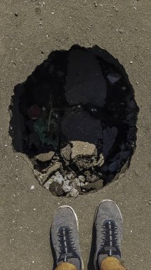 Yolda büyük derin saksı deliği. kuru kötü bakım. Trafik için tehlikeli. Araçlarda hasar var. derin deliğin yakınında manstand. 