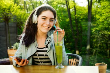 Kafede akıllı telefon kullanan genç güzel kadın, cam smoothie içme