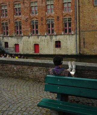 Şehrin meydanında merdivenlerde oturan, bir metin yazan ve müzik dinleyen genç adam.  