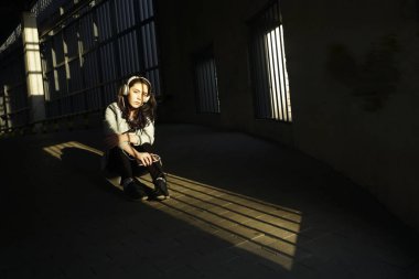 Neşeyle dinleniyor. Güzel genç kadın müzik dinliyor ve otoparkta yerde oturuyor. güneşli ışık ve yüzünde gölgeler